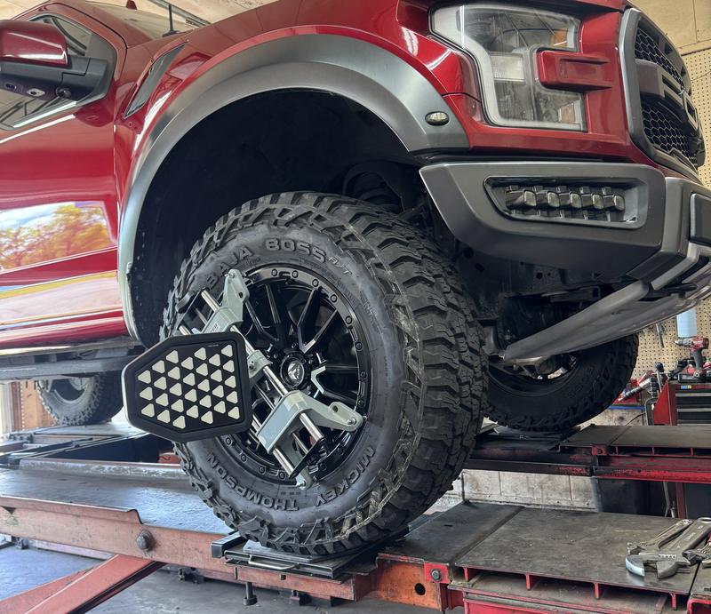 Red lifted pickup truck on the alignment rack with an alignment sensor clamped to the front wheel